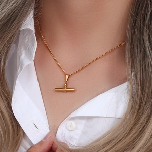 Close-up of gold T-bar pendant necklace worn with a white shirt for an elegant style
