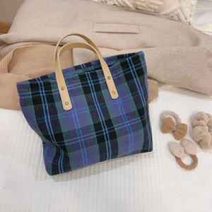 Close-up of retro plaid tote bag with leather handles and gold rivets on soft bedding