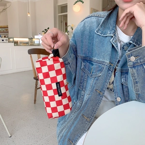 Detail shot of a red and white checkered corduroy pencil case with a merci paris label