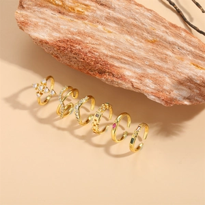 Cross and zircon gold ring set with wave and square stone designs on beige background