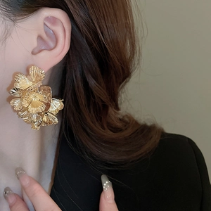 Gros plan d'un mannequin portant de grandes boucles d'oreilles fleurs dorées en métal