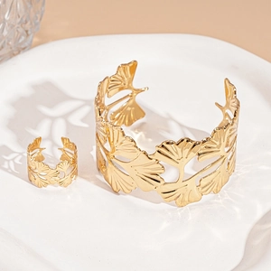 Detail of golden ginkgo leaf open bracelet and ring set on minimalist white ceramic plate