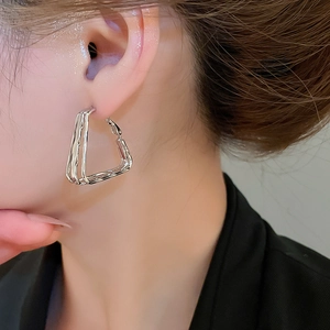 Close-up of geometric silver triangular hoop earrings on a female model wearing them