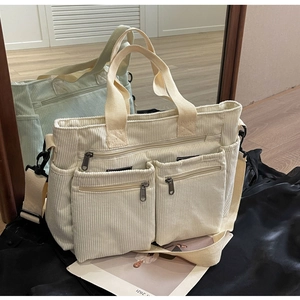 Detail view of cream corduroy shoulder bag featuring four front zippers and canvas straps