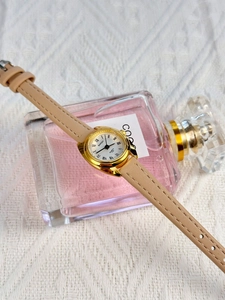 Detail of BARSH quartz watch with oval gold case and beige leather strap on perfume bottle