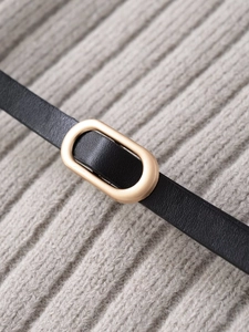 Detail of slim black leather belt with an oval gold buckle on a grey knit fabric