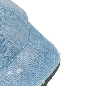 Detail of distressed light blue denim baseball cap showing embroidery and frayed brim texture