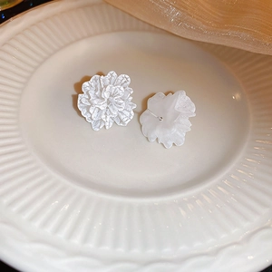 Detailed close-up of white floral stud earrings on an elegant white ceramic plate