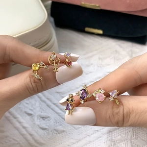 Macro detail of gold plated tiny earrings with colorful zircons held between fingers