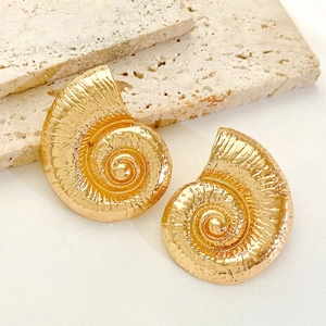 Macro shot of gold seashell earrings on beige travertine stone with elegant shadows