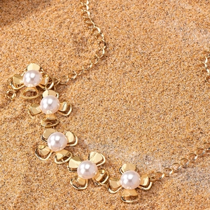 Elegant gold flower necklace featuring five white pearls on a natural sand background