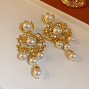 Detailed close-up of Baroque gold earrings with white pearls and sparkling rhinestones