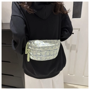 Detailed view of light green quilted crossbody bag with woven tassel zip pulls on model
