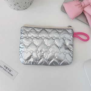 Detail of silver heart-quilted makeup pouch with pink zipper pull on white table