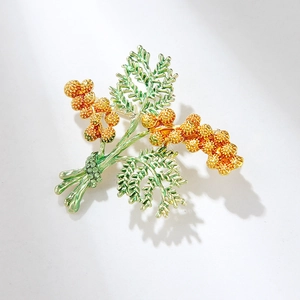 Elegant pine cone brooch with green enamel leaves and golden accents on a white background