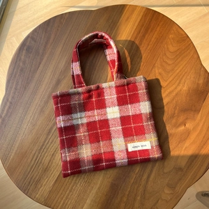 Gros plan du sac en laine à carreaux rouges sur table en bois avec étiquette tissée