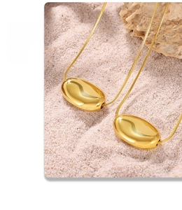 Golden bean pendant necklace on beach sand with sea shells for a luxury summer vibe