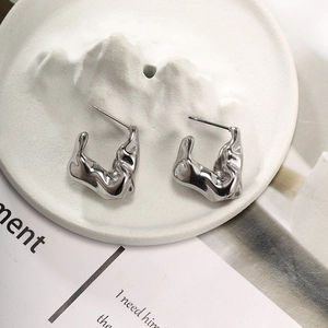Detailed macro shot of silver fluid lava earrings on a white porcelain mountain tray