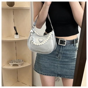 Macro view of silver metallic crescent bag featuring heart relief and large pearl strap