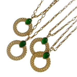 Minimalist gold chain necklace with round pendant and green oval gemstone on white background