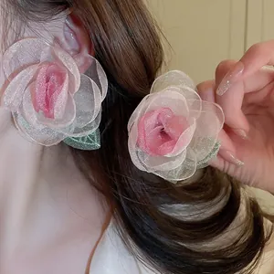 Macro detail of oversized layered pink mesh rose earrings with green leaf accents