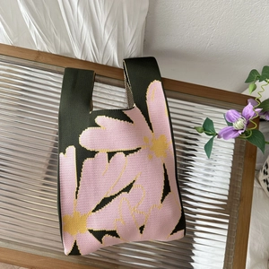 Close-up of green knitted tote bag with pink flower pattern on a glass table