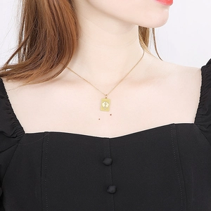 Detail of a gold rectangular zodiac pendant necklace worn on a woman's neck