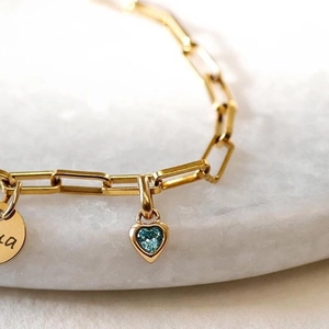 Gold chain bracelet featuring a blue sapphire heart pendant and round engraved charm