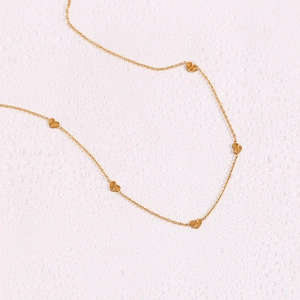 Detail view of a gold-plated stainless steel necklace with multiple heart charms on pink surface