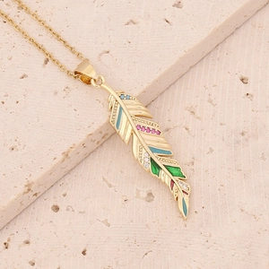 Close-up of golden feather pendant with colorful enamel and zircon on beige stone
