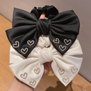 Close-up of satin bow scrunchies in black and beige featuring rhinestone heart details