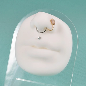 Silicone nose and mouth piercing model with gold zircon flower rings on blue background