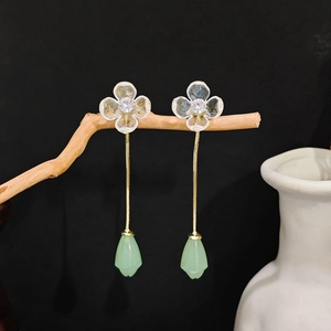 Detail of long floral tassel earrings with green teardrop pendants on wooden branch