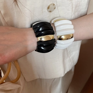 Close-up of wide acrylic bangles in black and cream white with gold metal accents
