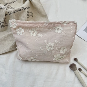 Detail of light pink makeup bag featuring white 3D floral embroidery and side brand tag