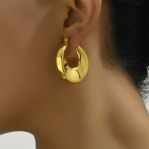 Close-up detail of polished gold hollow hoop earrings shown on a female model side profile