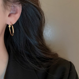 Close-up of a model wearing a minimalist golden geometric hoop earring on her ear