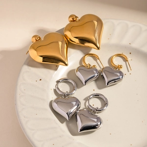 Elegant gold and silver heart-shaped earrings displayed on a textured ceramic plate