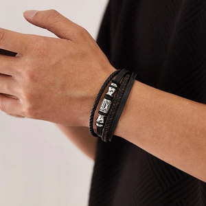 Close-up of multilayered black braided leather bracelet with silver metal charms on wrist