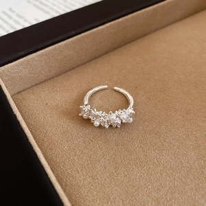 Detailed view of silver zircon and pearl cluster open ring on a beige jewelry box cushion