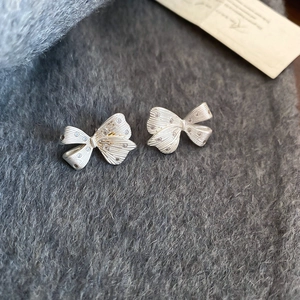 Detail of silver bow earrings with brushed metal texture and tiny crystals on grey fabric
