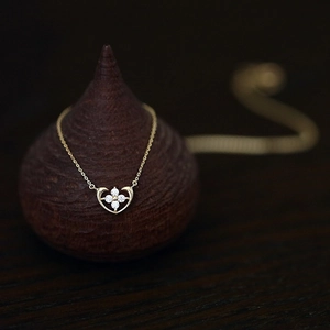 Detail of heart pendant with four-leaf flower inlay and white gems on gold chain