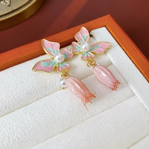 Dettaglio macro di orecchini vintage a farfalla in smalto rosa e verde con perle