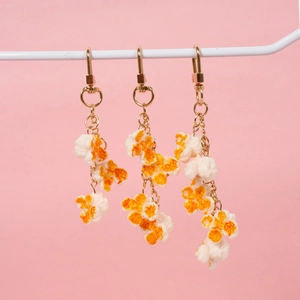 Realistic PVC popcorn keychains with golden lobster clasps on a pink background