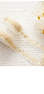 Close-up of cream sheer organza ribbon with elegant gold foil heart and vine patterns