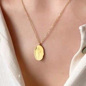 Detail of a gold stainless steel necklace with engraved floral pendant on a woman's neck