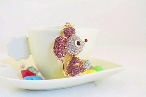 Macro shot of cute gold alloy mouse keychain with pink rhinestones by a white cup