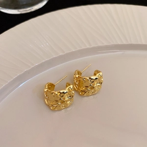 Close-up of golden heart earrings with wrinkled metal texture on a white plate