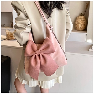 Close-up of pink suede bag featuring a large decorative bow and metal chain strap detail