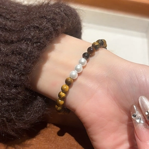 Detail of vintage tiger eye and pearl beaded bracelet worn on wrist with wool sleeve